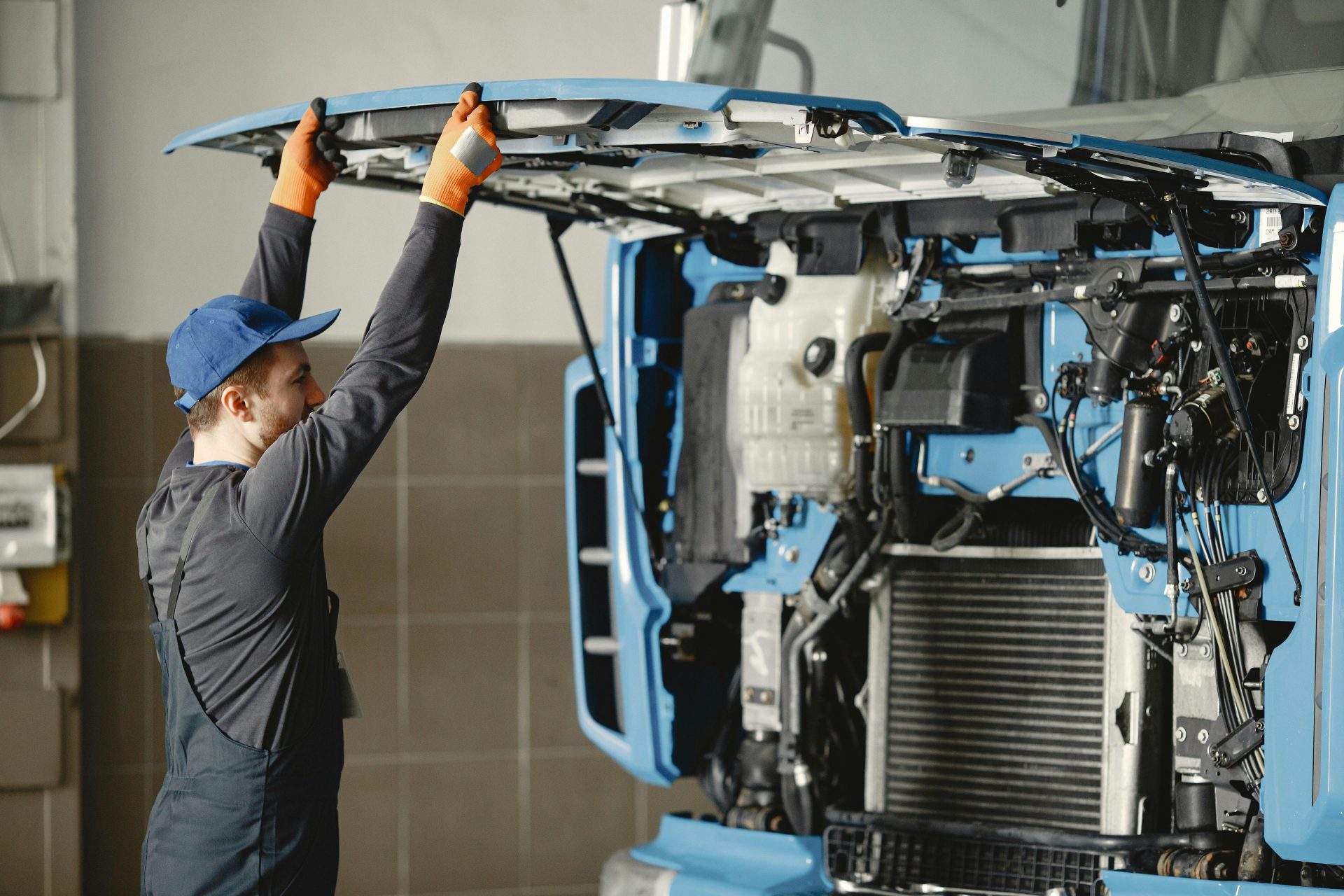 Ein Mechaniker in Uniform überprüft in einer Halle einen LKW-Motor auf Wartungsbedarf.